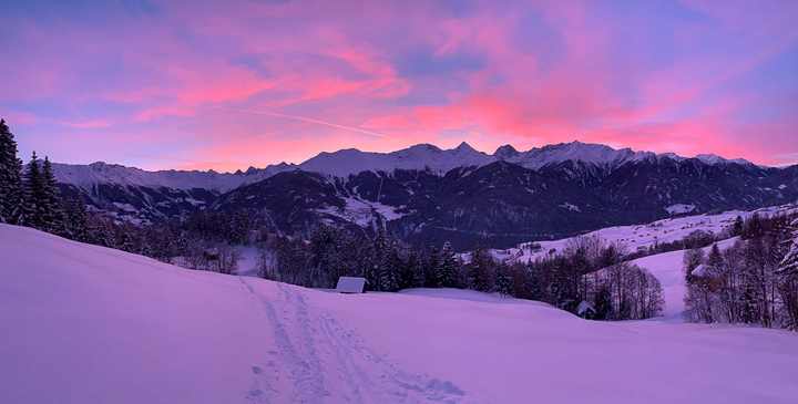 Dawn light over the mountains and a path through fresh snow